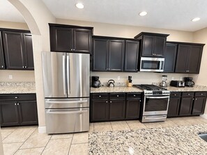 A kitchen with dark cabinets, stainless steel appliances, and a granite countertop. - Family-Friendly Luxury Villa | Sleeps 14 | Private Pool, Game Room & More! (Davenport)