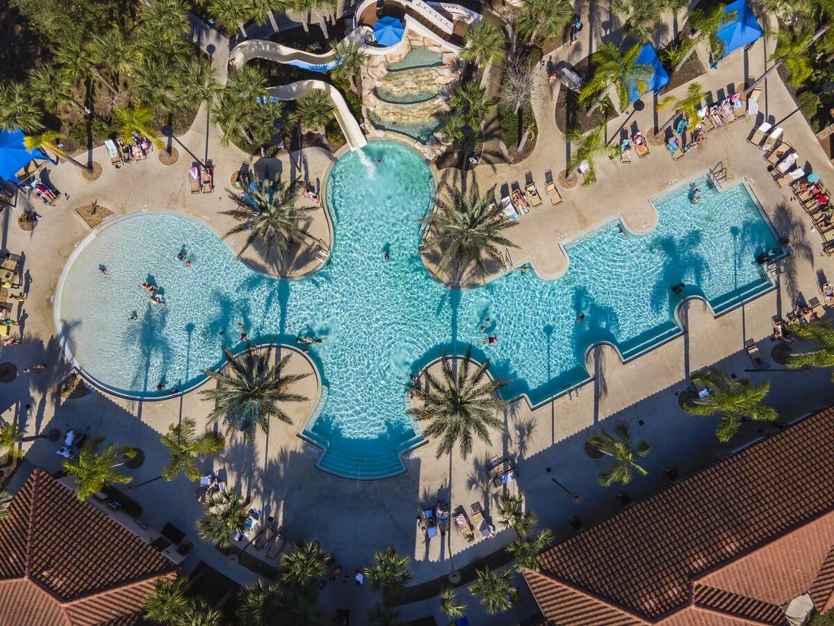 A large outdoor swimming pool with multiple sections and palm trees surrounding it.