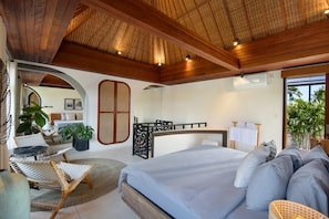 A bedroom with a large bed, a desk, and a chair. There is a window with a view of palm trees. - Villa Pawikan (Keroboken Kelod)
