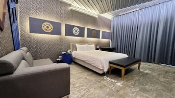 A hotel room with a bed, a sofa, a small table, and a wall with decorative elements.