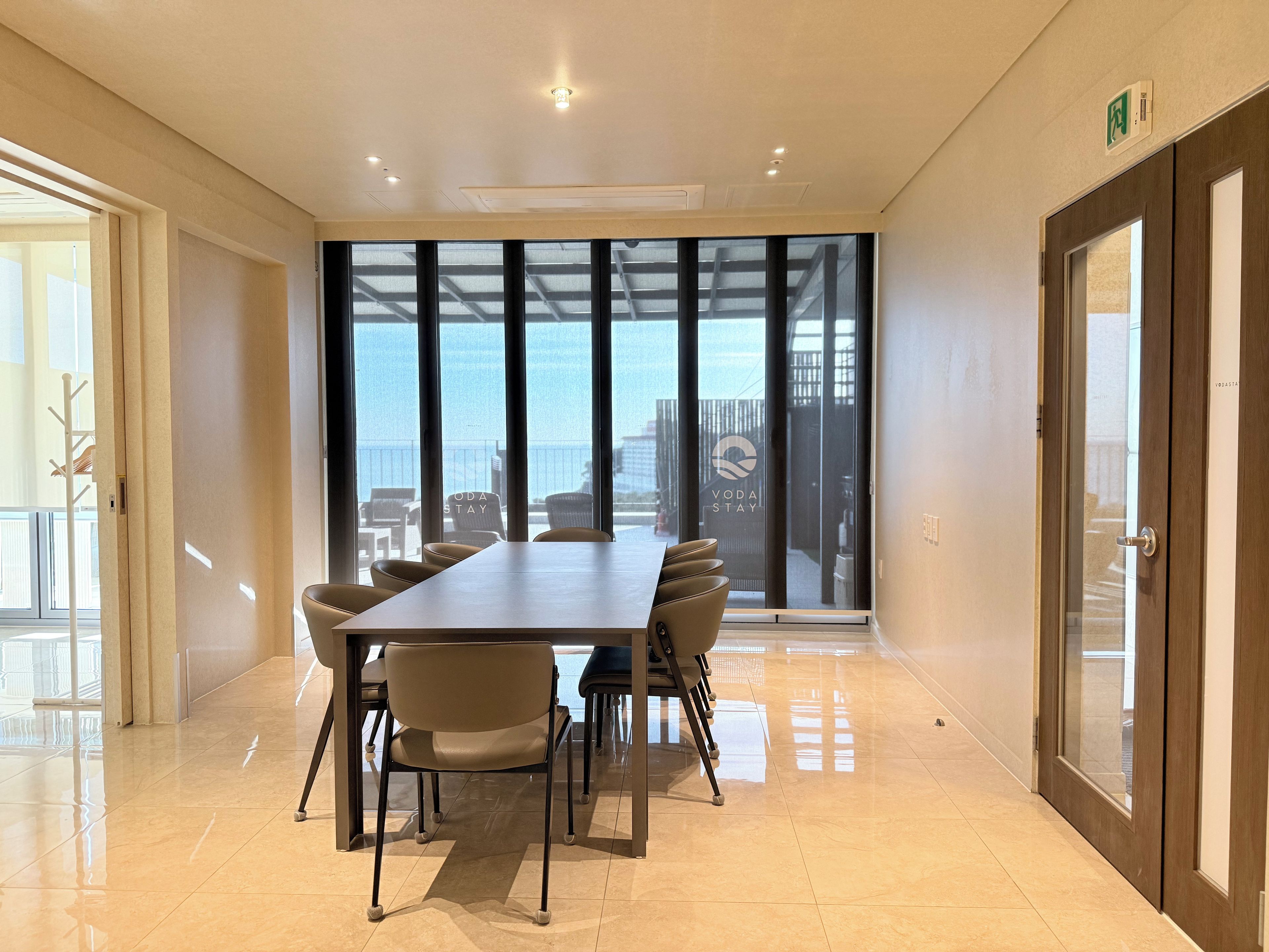 A conference room with a large table, chairs, and a view of the sea through floor-to-ceiling windows.