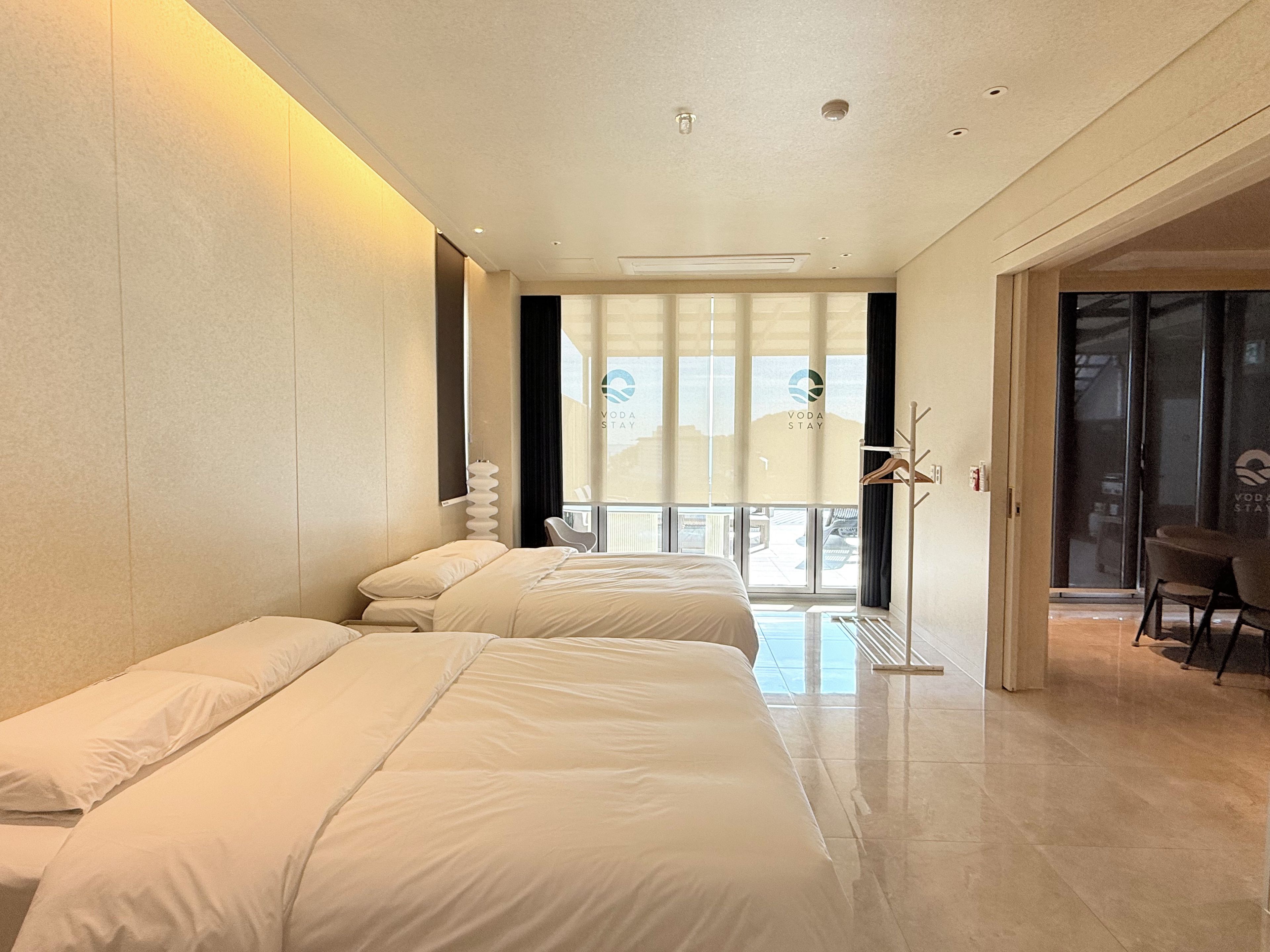 A hotel room with two beds, a seating area, and a view through the window.