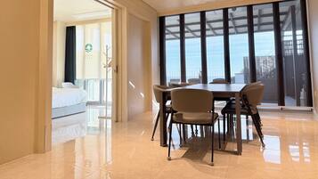 A hotel room with a bed, a dining area with a table and chairs, and a large window offering a view.