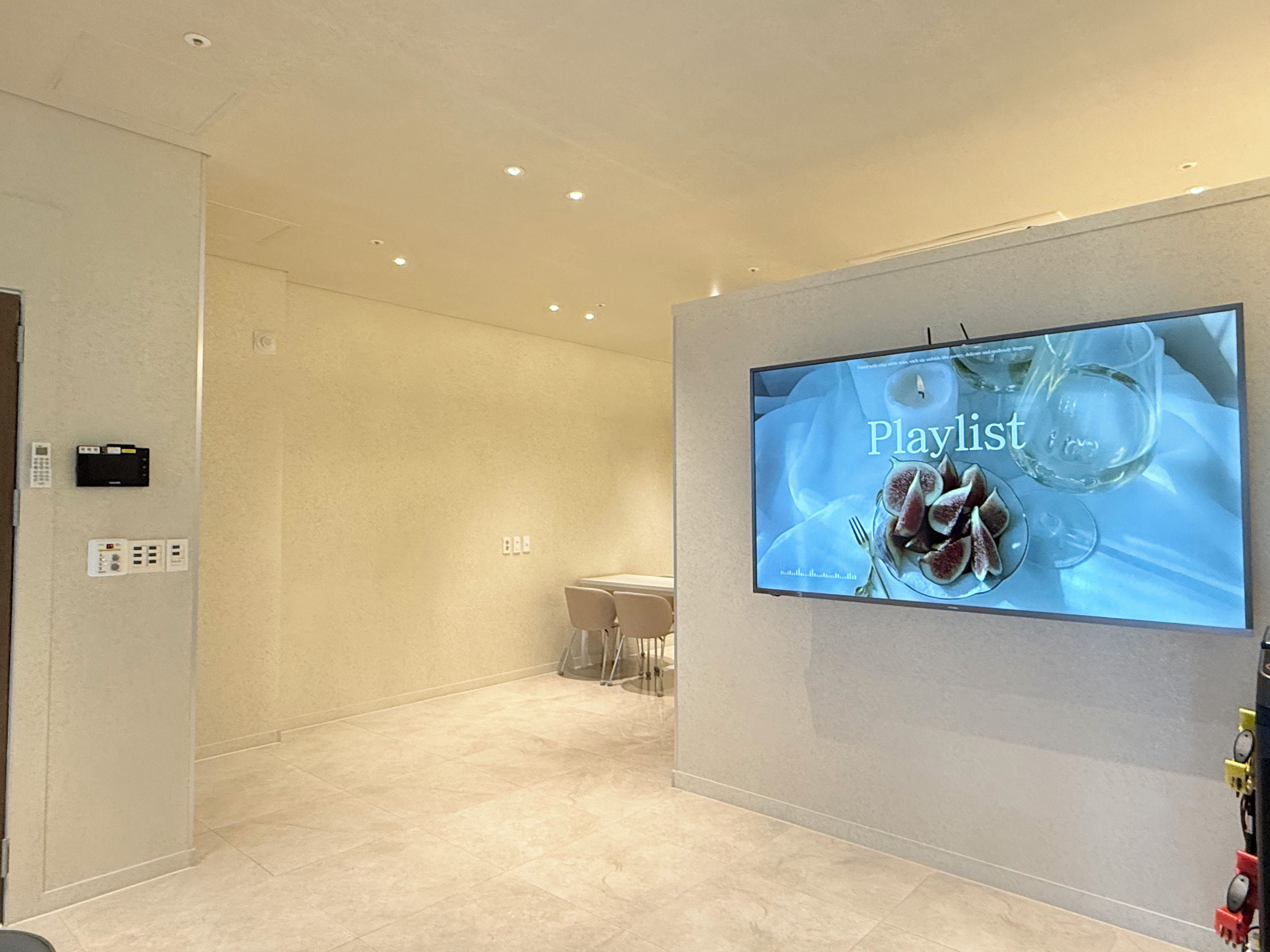Un hall d’hôtel moderne doté d’un téléviseur à écran plat diffusant une liste de lecture, d’un comptoir d’accueil et d’un design épuré et minimaliste.