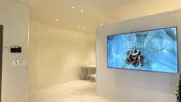 Un moderno vestíbulo de hotel con una televisión de pantalla plana mostrando una lista de reproducción, una recepción y un diseño limpio y minimalista.
