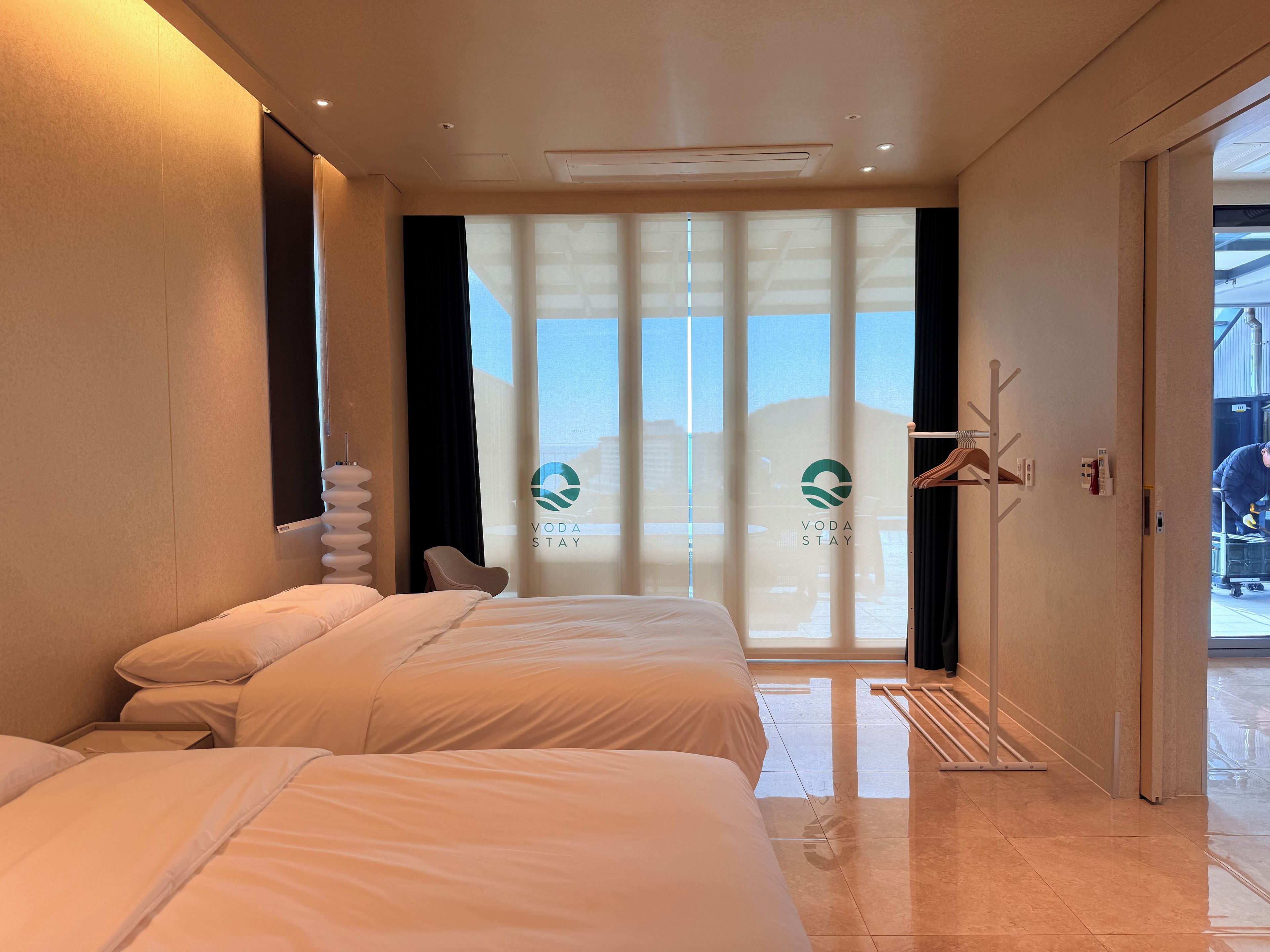Una habitación de hotel con dos camas, un ventanal con vistas y una puerta que da a un balcón.
