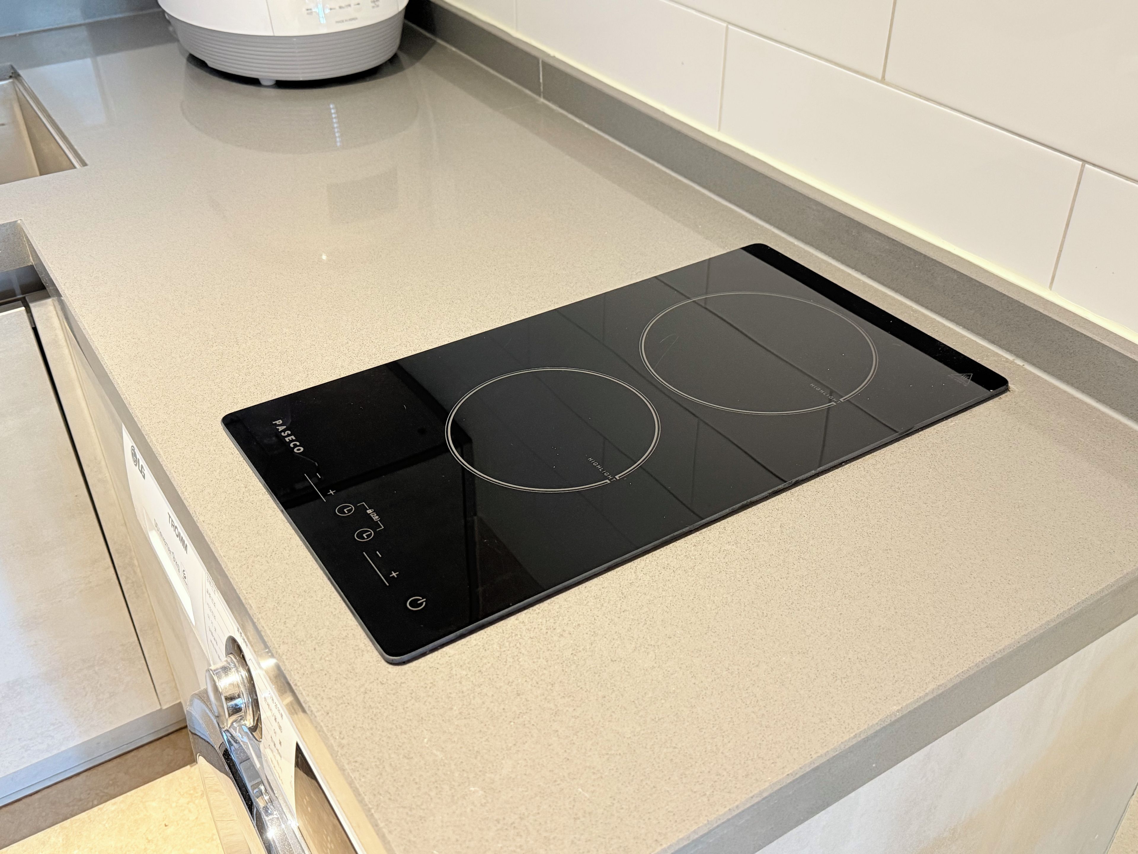Una cocina con una placa de inducción negra y un electrodoméstico blanco al fondo.