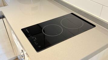 Una cocina con una placa de inducción negra y un electrodoméstico blanco al fondo.