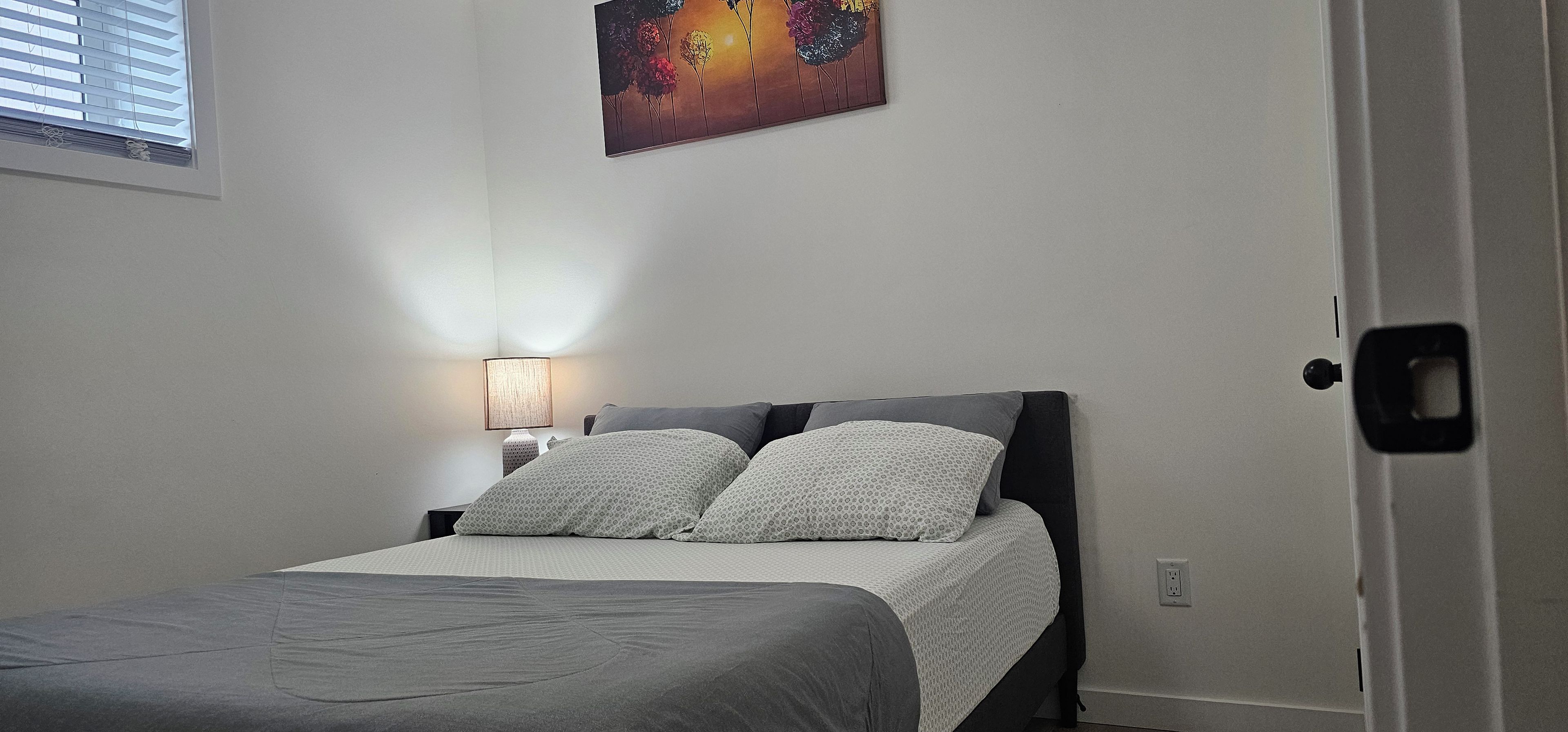 A bedroom with a bed, a nightstand, a lamp, and a painting on the wall.