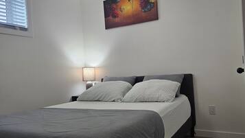 A bedroom with a bed, a nightstand, a lamp, and a painting on the wall.