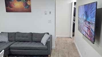 Een moderne woonkamer met een hoekbank, een flatscreen-tv aan de muur en een kleurrijk abstract schilderij erboven.