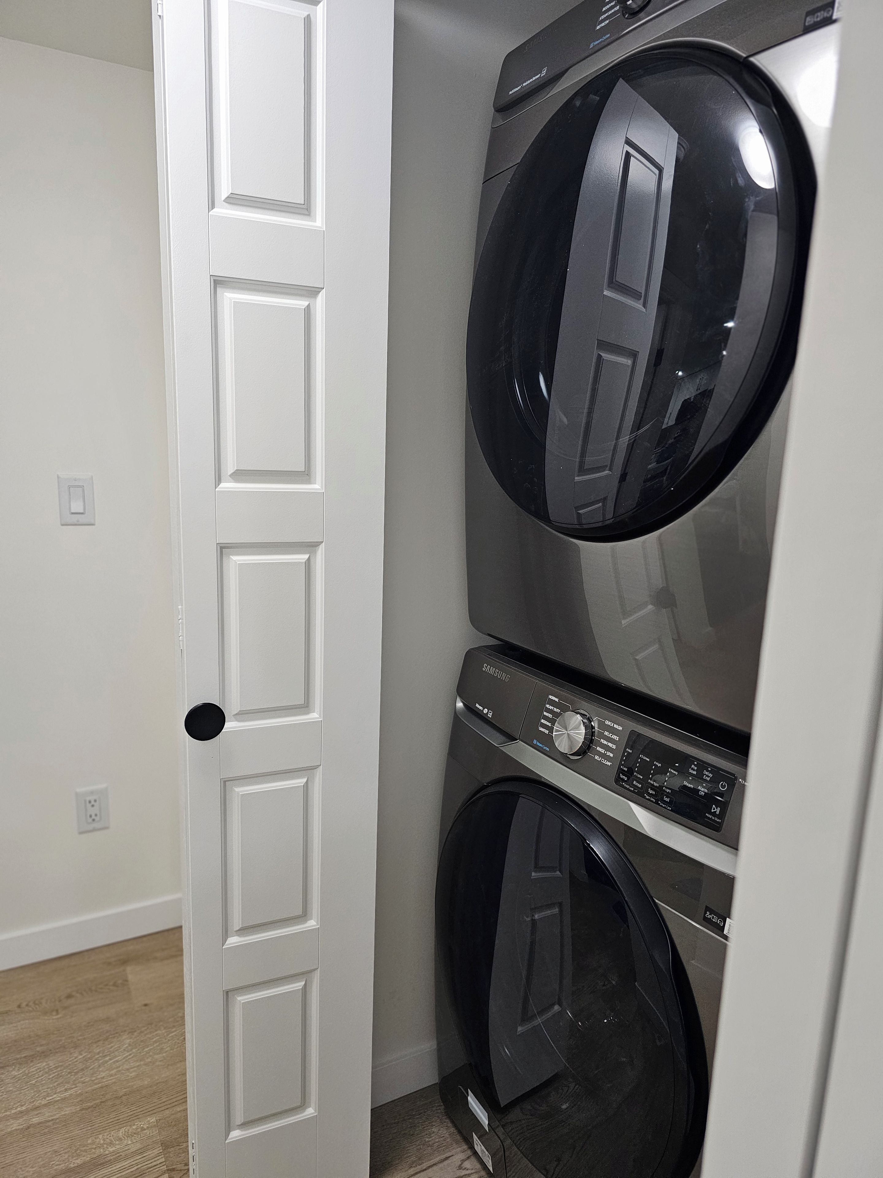 A laundry room with two stacked front-loading washing machines and a white door.