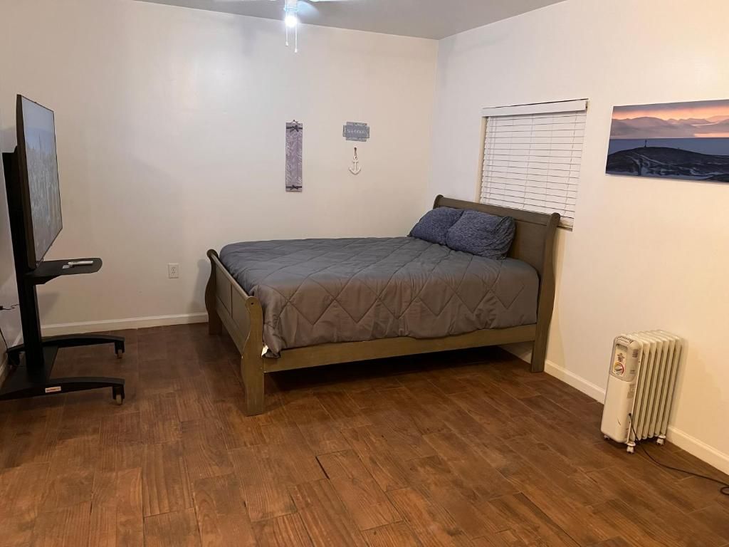 A bedroom with a bed, a desk, a radiator, and a wall-mounted TV.