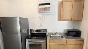 Une cuisine compacte équipée d’un réfrigérateur, d’une cuisinière, d’un four à micro-ondes et de meubles de rangement en bois.