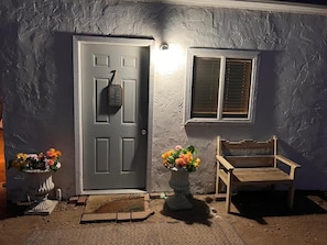 A house with a gray door, a window with blinds, a bench, and two flower pots. - Moreland Guesthouse (Phoenix)