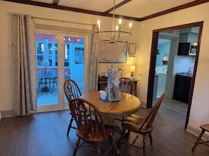 A dining area with a wooden table and chairs, a chandelier, and a view of the outside.