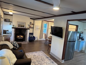 A living room with a fireplace, a television, and a kitchen area with a refrigerator.