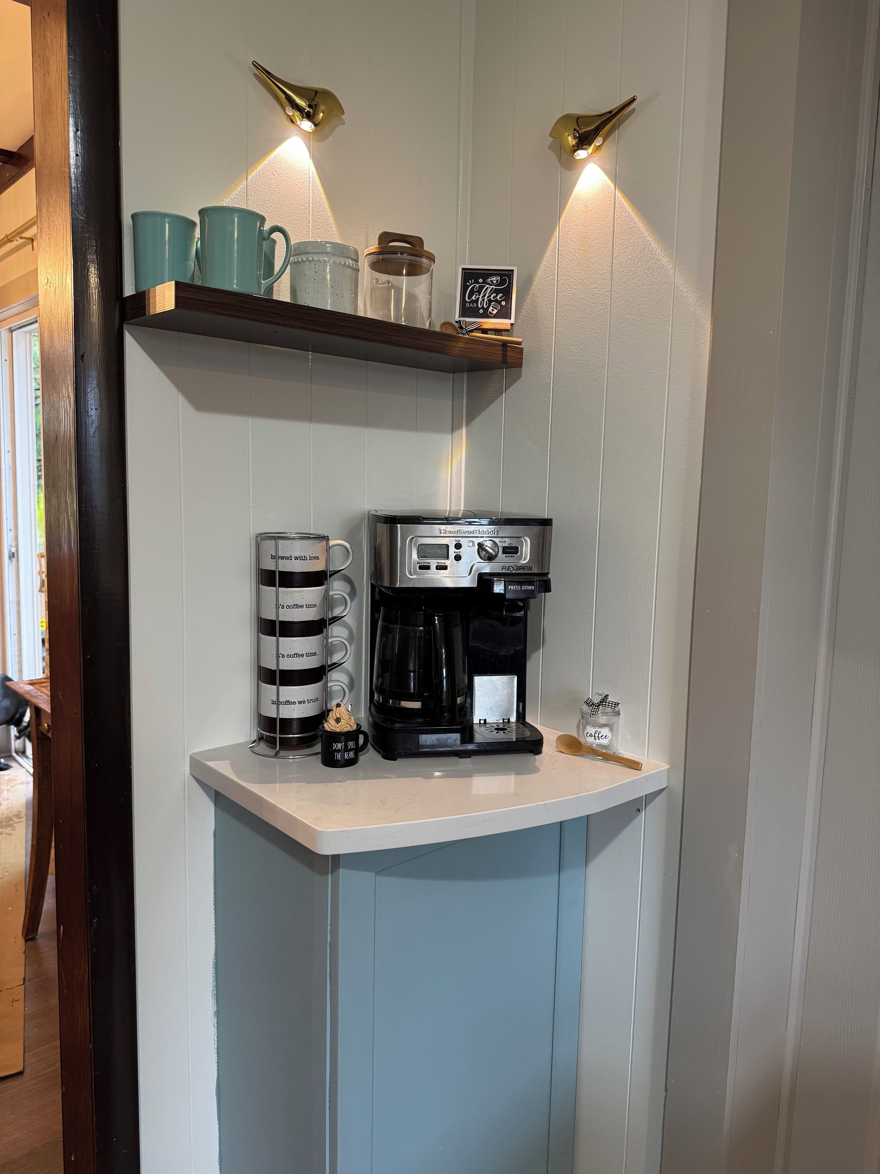 A kitchenette with a coffee maker, mugs, and a coffee-themed sign.