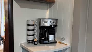 A kitchenette with a coffee maker, mugs, and a coffee-themed sign.