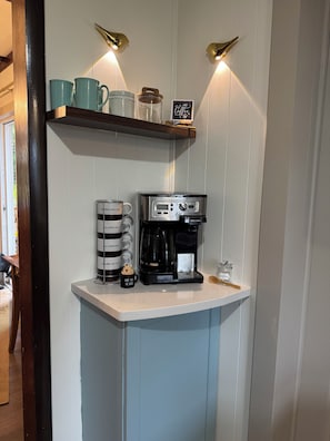 A kitchenette with a coffee maker, mugs, and a coffee-themed sign.