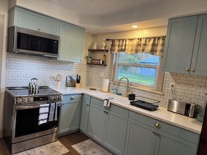 A modern kitchen with a stainless steel range, a microwave, and a built-in oven. There is a window with a view of the outdoors, and the kitchen has light blue cabinets and white countertops.