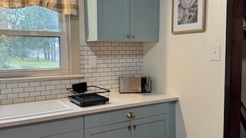 A kitchen with light blue cabinets, a white countertop, a toaster, and a window with a view of trees.