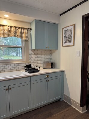 A kitchen with light blue cabinets, a white countertop, a toaster, and a window with a view of trees.