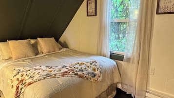 A bedroom with a bed, a window with curtains, a wall-mounted picture, and a textured rug.