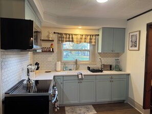 A kitchen with white tiled backsplash, a stove, a sink, and a window with a view of the outdoors.