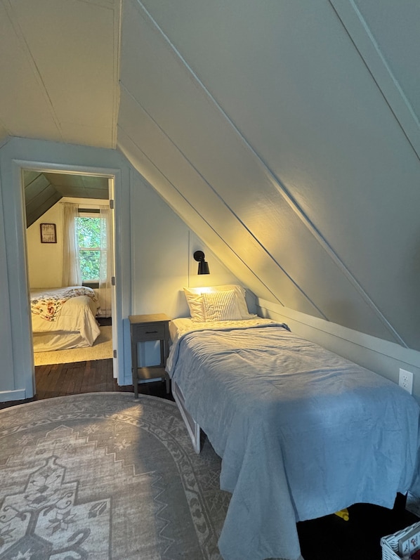 A bedroom with a sloped ceiling, a bed, a bedside table, and a nightstand. - Rickett's Cozy Cottage in Lopez PA- Pet Friendly (Lopez)
