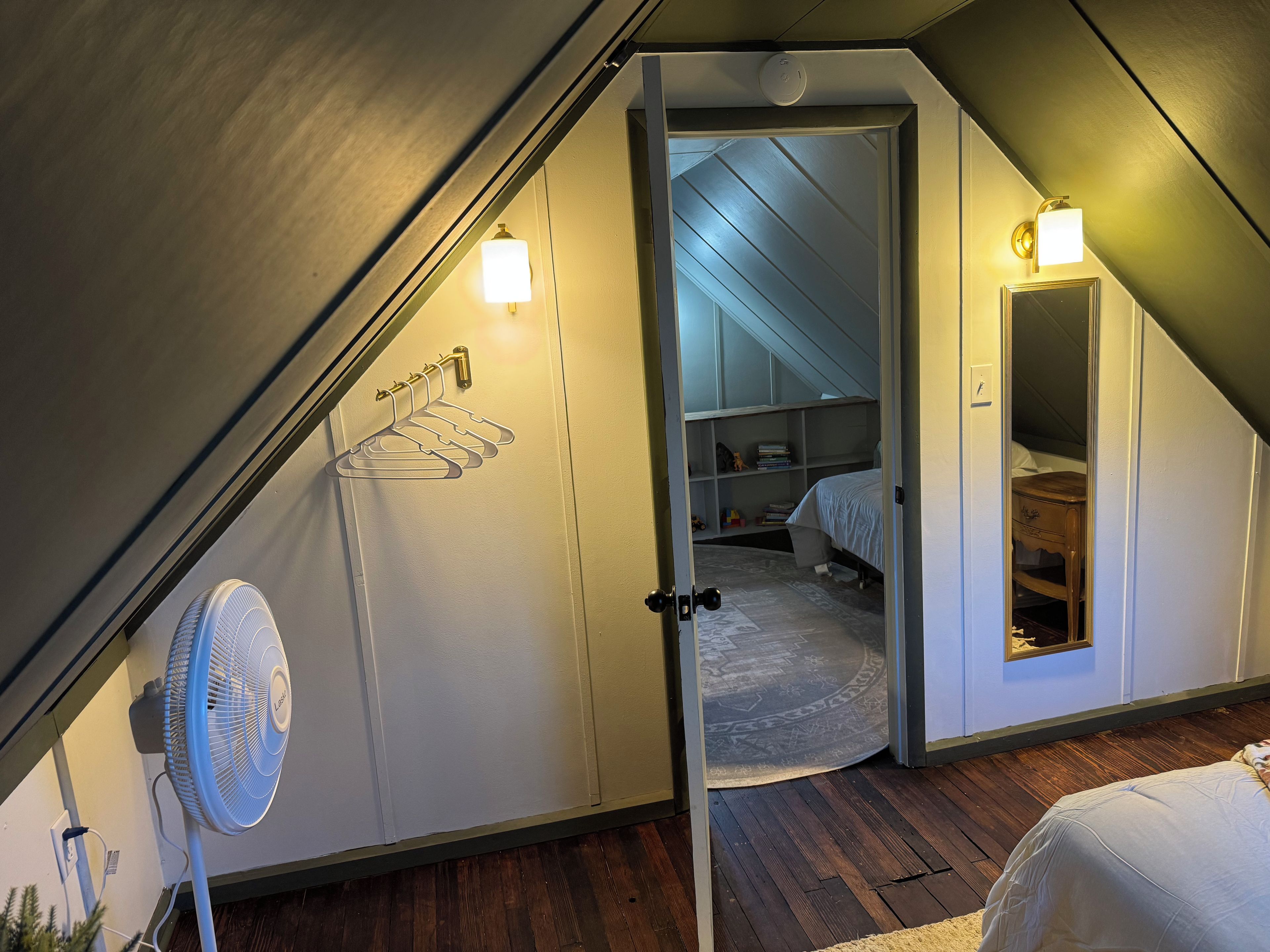 A bedroom with a sloped ceiling, a bed, a fan, and a walk-in closet.