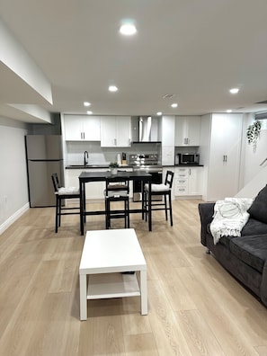 A modern kitchen with white cabinets, a central island, and a dining area with a white table and chairs.