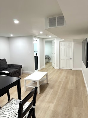 Un salon moderne avec un canapé, une table à manger et une table basse. Un couloir mène à une porte.