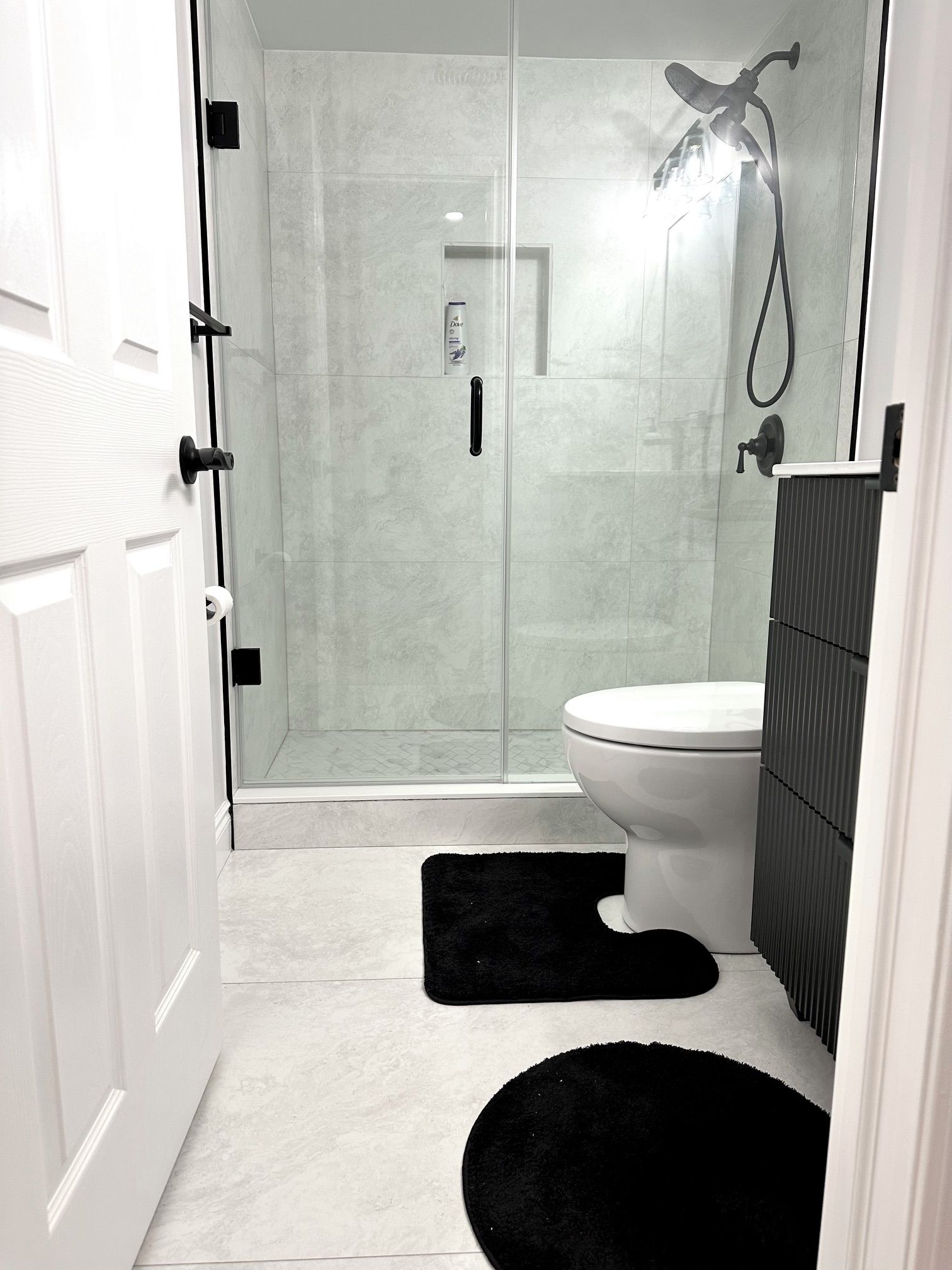 Une salle de bain moderne avec une douche à parois de verre, des toilettes et un tapis noir.
