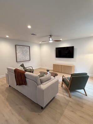 A modern living room with a sofa, armchairs, a coffee table, a TV, and a ceiling fan. - Renovated 3 Bed/2 Bath Austin Retreat Minutes from Downtown, Domain & Airport (Austin)