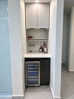 Eine kleine Küchenzeile mit integriertem Mini-Kühlschrank, einer Mikrowelle und einem Regal mit Gläsern und Flaschen.
