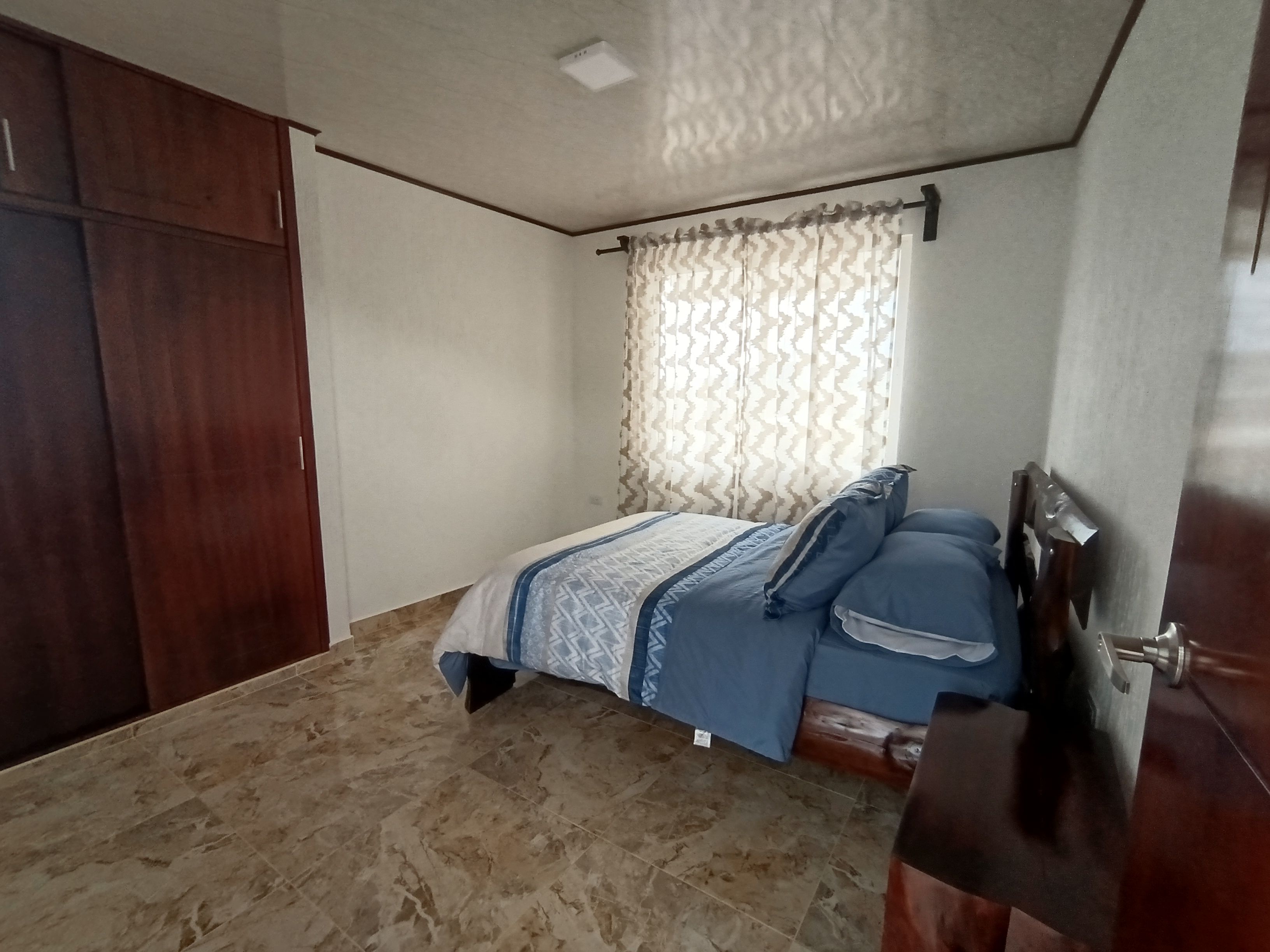 A bedroom with a bed, a wardrobe, and a window with curtains.