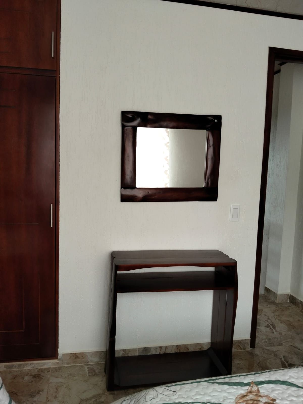 A room with a wooden wardrobe, a wooden console table, and a mirror on the wall.