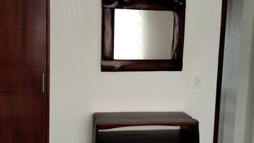 A room with a wooden wardrobe, a wooden console table, and a mirror on the wall.