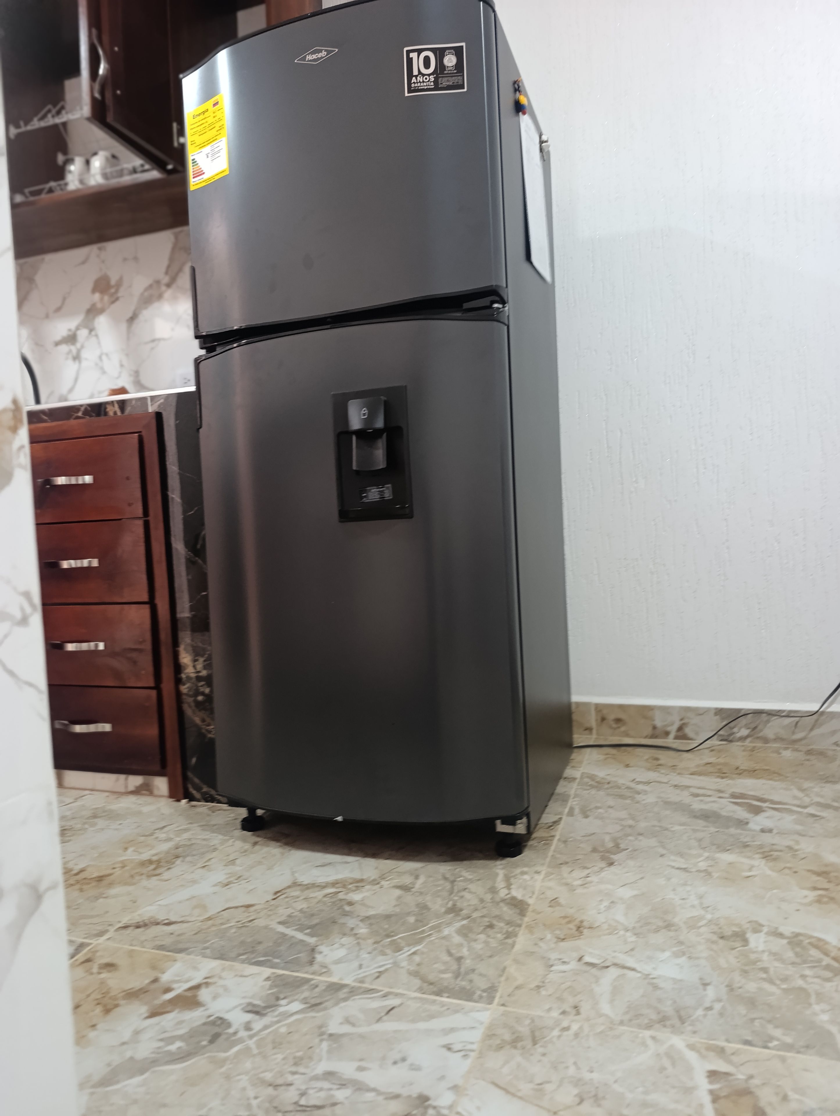 A black refrigerator with a water dispenser, a 10-year anniversary sticker, and a control panel.