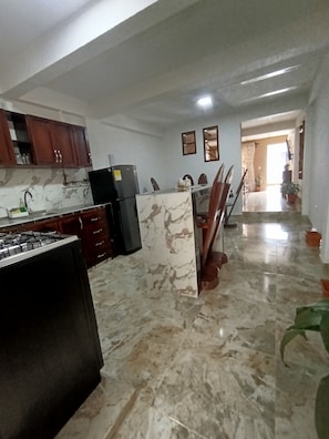 Una cocina con estufa a gas, armarios, refrigerador y un comedor con sillas y una mesa.