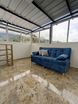 A room with a blue sofa, a wooden ladder, and large windows offering a view of the outdoors. - Casa LuzErick hospedaje  (Calima)