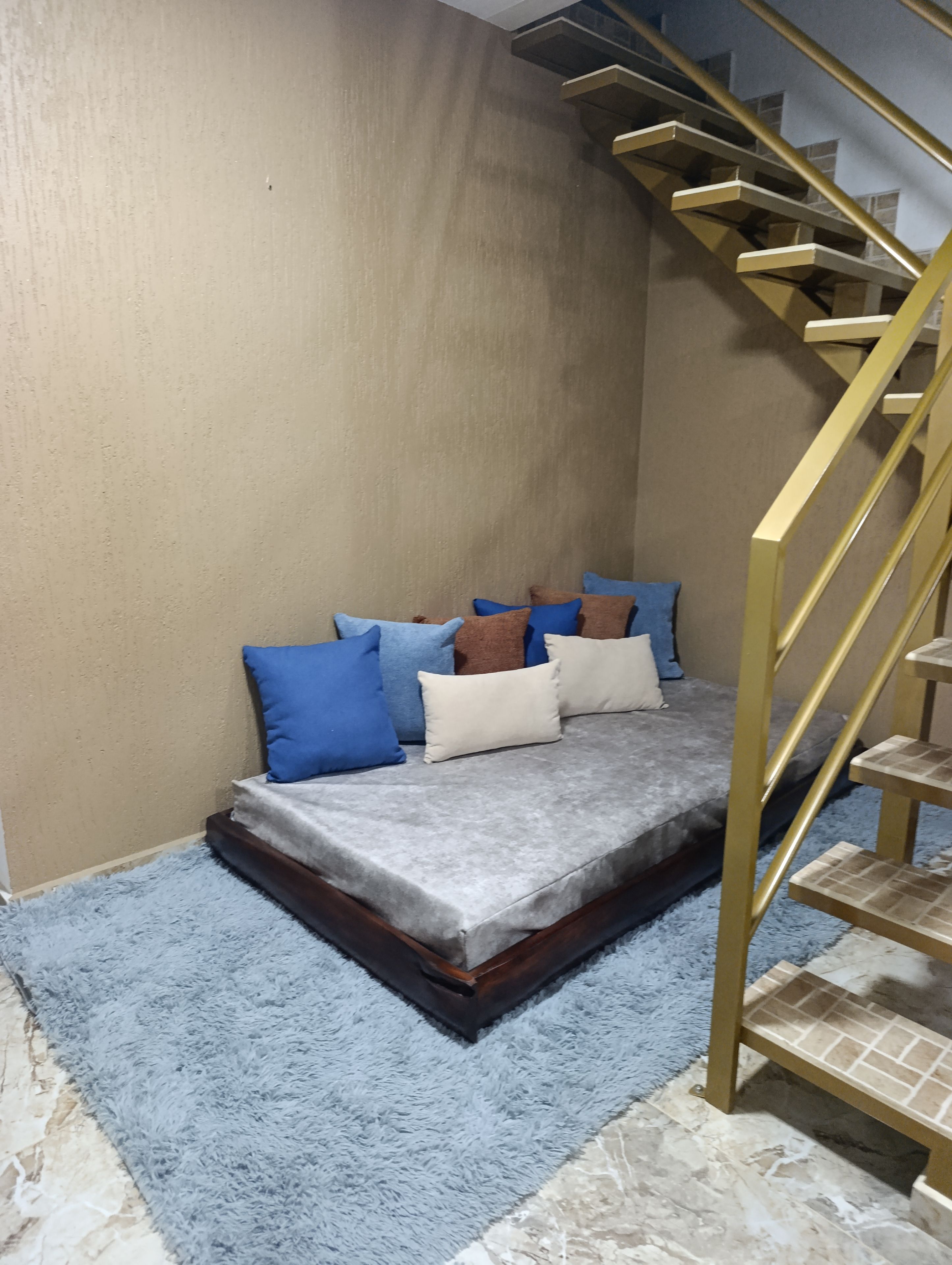 Une pièce avec un lit, un tapis bleu, un escalier et un mur.