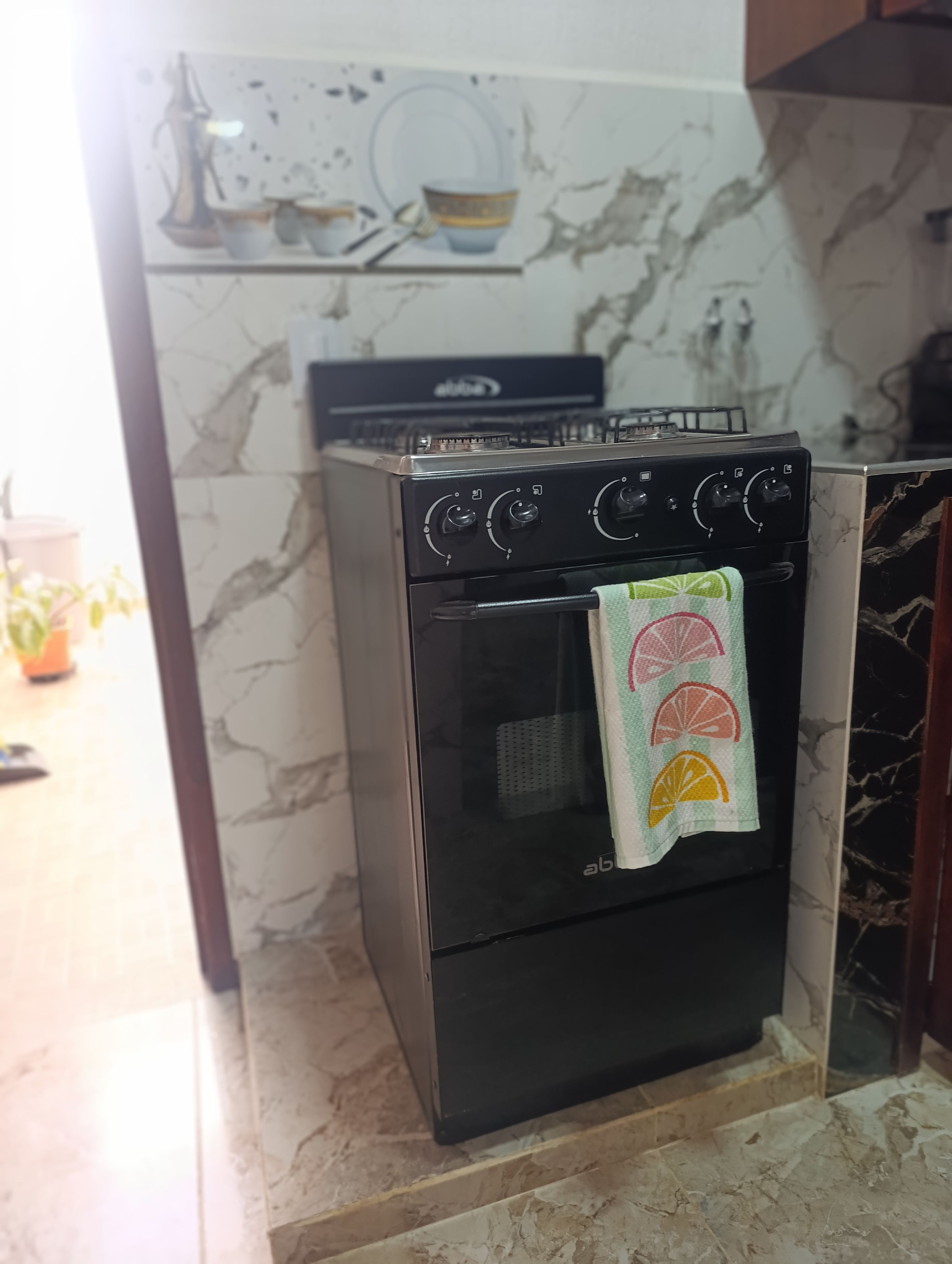 Una cocina con horno negro, salpicadero de mármol y una toalla con motivos de cítricos.