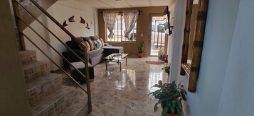 Una sala de estar con una escalera, un sofá, una mesa de centro y una puerta que da al exterior.