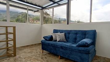 A room with a blue sofa, a wooden ladder, and large windows offering a view of the outdoors.