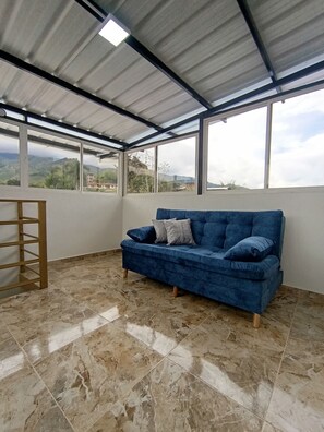 Una habitación con un sofá azul, una escalera de madera y grandes ventanales con vistas al exterior.