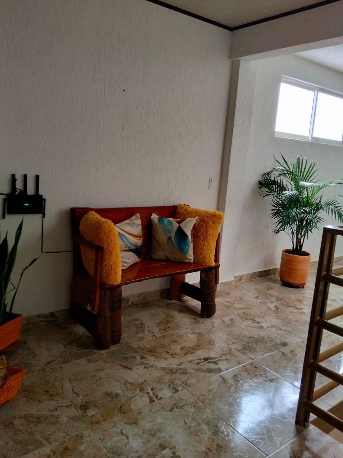 A room with a wooden bench, a potted plant, and a tiled floor.