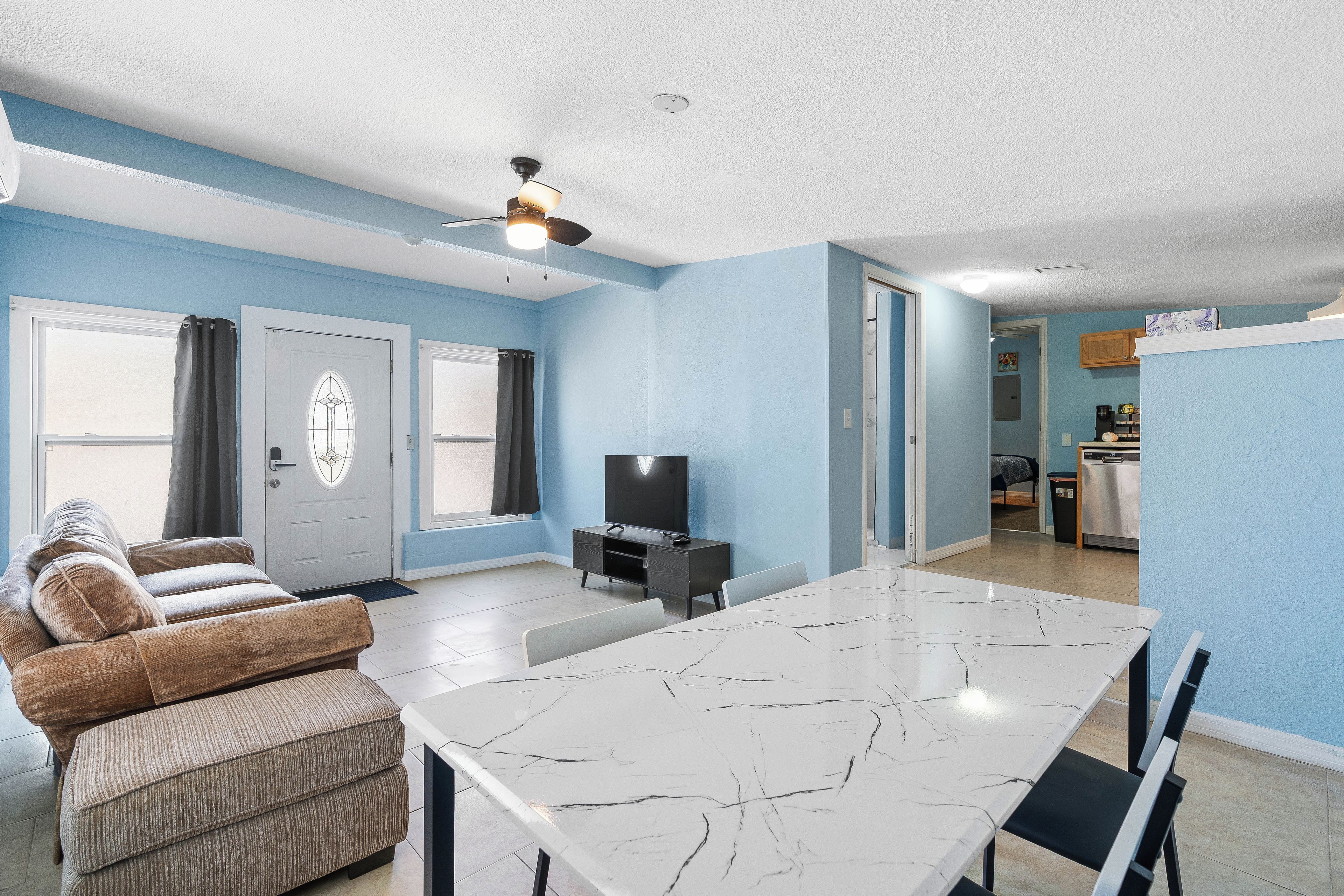 A modern living room with a dining table, sofa, and a ceiling fan.