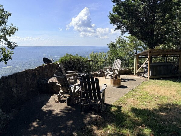 A patio with Adirondack chairs, a fire pit, and a view of the ocean.